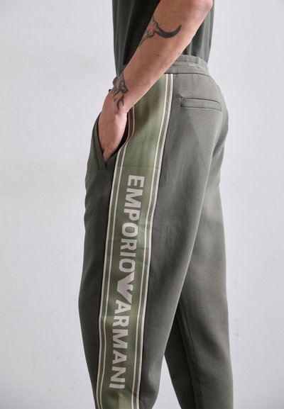 Sivé-zelené teplákové nohavice s úzkym strihom. Obsahujú bočný pruh s nápisom "EMPORIO ARMANI" v bielej farbe a vrecko na pravej strane.