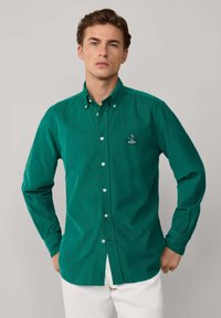 Grüne Baumwollhemd mit langen Ärmeln, Button-Down-Kragen und einem gestickten Logo auf der linken Brust.