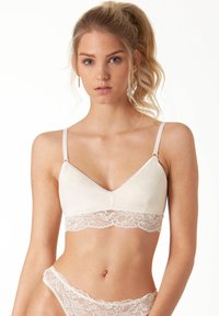 Brassière con parte superiore in satin beige chiaro e fascia inferiore in pizzo. Dotata di spalline regolabili e design a V. Texture morbida.