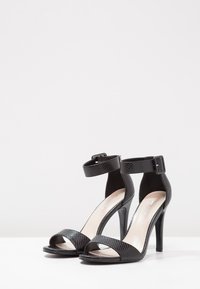 Sandales à talons hauts noires avec un motif texturé inspiré des reptiles, une conception à bout ouvert et une bride réglable à la cheville avec une boucle.