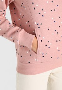 Felpa rosa con finitura testurizzata, caratterizzata da un motivo di piccoli diamanti multicolori. Include una tasca frontale e polsini a costine.