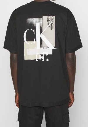 Personne portant un T-shirt noir avec des blocs abstraits blancs et beiges et le texte "Calvin Klein Jeans New York Est. 1978" dans le dos.