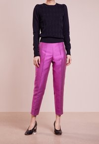 Black textured sweater with diamond pattern, paired with high-waisted, shiny pink trousers. Black pointed-toe heels complete the outfit.