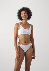 Hvitt undertøy sett bestående av en trekantet bralette og bikinibukser. Bh-en har et gjennomsiktig meshinnlegg; buksene har en mønstret livlinje.