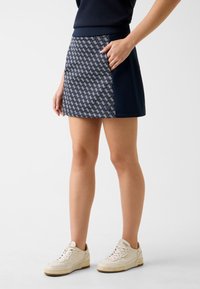 Granatowy skort w geometryczny wzór, z jednolitym granatowym bocznym panelem i boczną kieszenią. W zestawie z białymi trampkami.