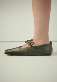 Grønne ruskindsballerinaer med spidse tæer, en udskæring foran og to bundne detaljer ved anklen. Flad sål.