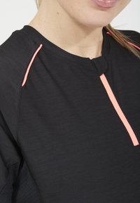 Svart idrottströja med rund hals, subtil textur och kontrasterande rosa accent längs fram- och axelsömmarna.