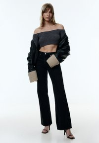 Schwarze Lederjacke mit beigefarbenen Fleece-Manschetten, graues gestricktes Cropped-Top und schwarze ausgestellte Jeans. Offene schwarze High Heels runden das Outfit ab.