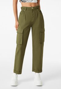 Olivově zelené cargo kalhoty s vysokým pasem, dvěma bočními kapsami a ohrnutými manžetami. Vyrobené z bavlny, s knoflíkovým zapínáním a kovovými akcenty.