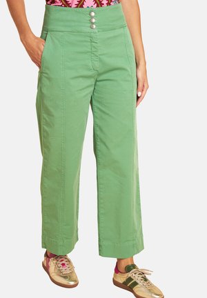 Woman wearing high-waist green wide-leg pants with front buttons and beige sneakers with pink and green accents.