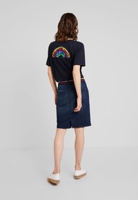 Camiseta navy con gráfico de arcoíris pixelado en la parte posterior, combinada con una falda de mezclilla oscura que cuenta con bolsillos traseros y un diseño hasta la rodilla.