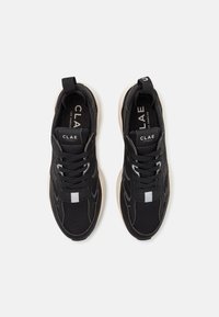Black sneakers with mesh and suede materials, featuring a light grey sole, contrasting laces, and logo on the tongue and side.