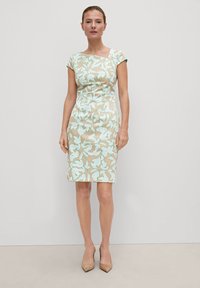 Figurbetontes Kleid aus beigem Stoff mit floralem Minzmuster, kurzen Ärmeln und asymmetrischem Ausschnitt, das knapp über dem Knie endet.