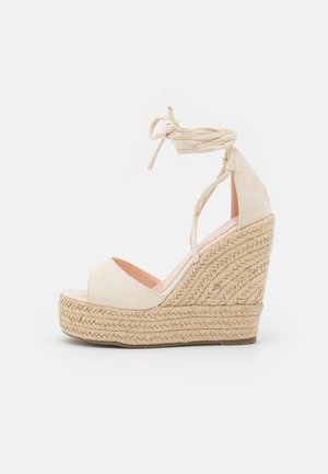 Sandale compensée beige avec plateforme en jute tressé et lanières à nouer autour de la cheville.