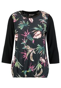 Musta pitkähihainen paita, jossa on värikäs trooppinen kukkakuosi edessä, kerroshäntä ja kiinteät mustat hihat.