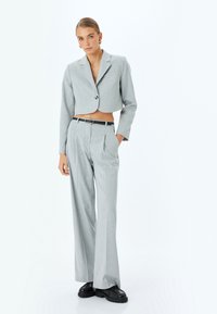 Blazer gris corto con un botón, combinado con pantalones grises de pierna ancha y cintura alta. Presenta un cinturón negro y zapatos negros gruesos.