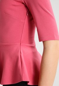 Rosa Peplum-Top mit kurzen Ärmeln, rundem Ausschnitt und seitlichem Nahtdetails. Hergestellt aus einem weichen, dehnbaren Stoff mit glatter Textur.