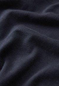 Tmavě námořnická tkanina s hladkým povrchem, která má jemné, subtilní vrásky a lehký vzhled, zdůrazňující její pružnost.