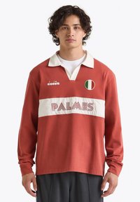 Maglietta da rugby a maniche lunghe rossa con pannello orizzontale bianco, presenta la scritta "PALMES" e un'emblema della bandiera italiana. Realizzata in cotone con un design con colletto.