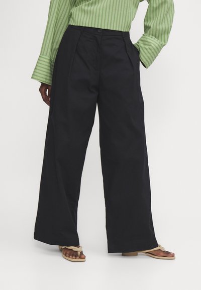 Grote zwarte broek gemaakt van lichtgewicht stof, met een hoge taille, plooien aan de voorkant en een knoopsluiting, gestyled met een groen gestreefd shirt.