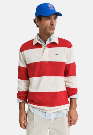 Rood-witte gestreepte polo met lange mouwen en een blauwe pet. Heeft een kraag en daaronder een lichtblauw geruit shirt in lagen.