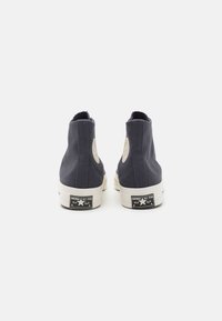 Námořnické vysoce špičaté plátěné tenisky s bílou gumovou podrážkou, s kruhovou nášivkou loga a značením Converse na patě.