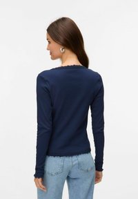 Marinblå långärmad topp med texturerad yta och spetsdetaljer vid halsringningen och fållen. Kombinerad med ljusblå denimjeans.