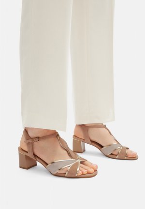 Sandales à brides beige et métalliques avec un petit talon carré ; comprennent un design à bride en T et des textures lisses avec bout ouvert et boucle à la cheville.