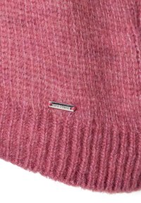 Gebreide roze beanie met ribbelstructuur en een zilverkleurig metalen label met de merknaam. Zacht wolachtig materiaal met subtiele kleurvariaties.