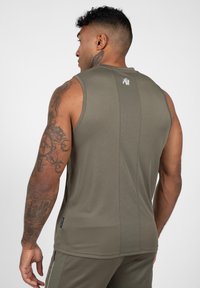 Olijfgroene mouwloze sportshirt met een gladde textuur, voorzien van een klein logo op de rug en stikseldetails langs de halslijn.