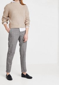 Beige stickad tröja med ett strukturerat, diagonalt mönster. Grå rutiga skräddarsydda byxor. Svarta loafers. Vit skjorta synlig under tröjan.