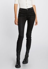 Jeans negros ajustados con una textura suave, que cuentan con bolsillos con cremallera y un cierre de botón, combinados con botas negras hasta el tobillo.