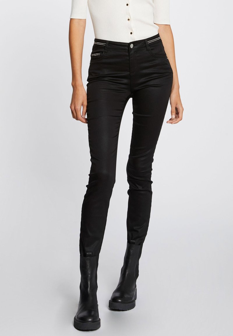 Jeans negros ajustados con una textura suave, que cuentan con bolsillos con cremallera y un cierre de botón, combinados con botas negras hasta el tobillo.