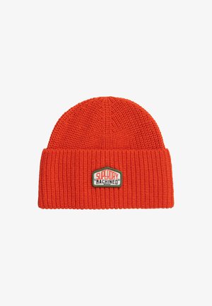 Bonnet tricoté orange vif avec bord replié présentant un patch rectangulaire portant l'inscription "SUPERDRY MACHINED" en texte rouge et noir.