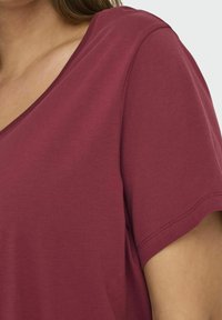 Bordeaux T-shirt met korte mouwen, voorzien van een V-hals en een zachte katoenstof, met zichtbare stikseldetails op de mouwen en de zoom.