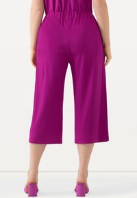 Pantaloni culotte fucsia con vita elasticizzata, lunghezza cropped e texture liscia, abbinati a sandali con tacco a blocco coordinati.
