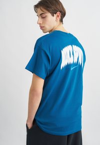 Μπλε βαμβακερό T-shirt με λευκή εκτύπωση γραφικών κειμένου "WILD SPORT" στην πλάτη, κοντά μανίκια και χαλαρή εφαρμογή.