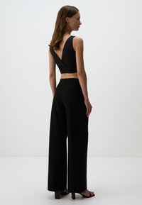 Haut sans manches noir avec un dos en V profond, associé à un pantalon noir à jambes larges et des sandales à talons carrés, avec une texture lisse.