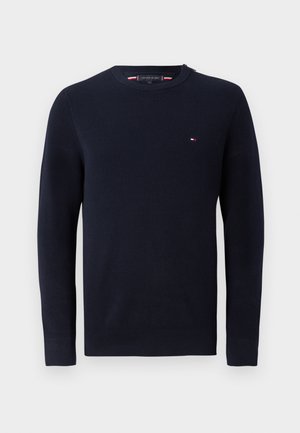 Suéter de algodón azul marino con punto texturizado, cuello redondo y mangas largas. Presenta un pequeño logotipo en rojo, blanco y azul en el pecho.