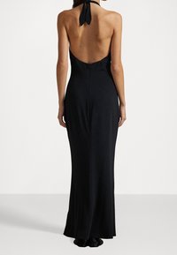 Svart halterneck-klänning med djup rygg, åtsittande silhuett och dragkedja. Slätt tyg med golvlång design.