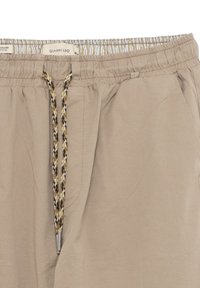 Pantaloni corti color beige chiaro con cintura elastica, dotati di un cordoncino fantasioso e tasche laterali, realizzati in un tessuto liscio e leggero.
