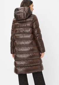 Brun pufferjakke med hætte og syet, quiltet mønster. Materialet ser skinnende ud og har en lang pasform, der når til midt på låret.