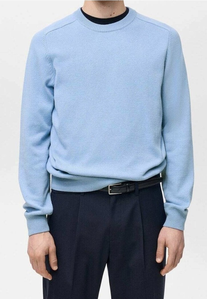 Hellblauer, gestrickter Rundhalspullover mit einem gerippten Kragen und Saum; kombiniert mit dunklen Hosen, die einen schwarzen Gürtel haben. Glatte Textur.