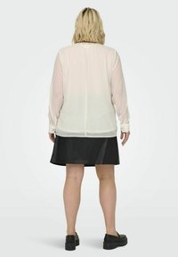 Lyserød, prikket skjorte med lange ærmer, parret med en sort nederdel. Outfittet har en blød tekstur og en afslappet pasform.