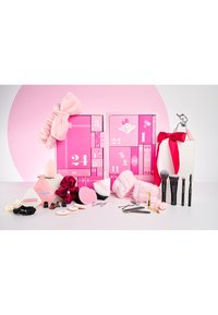 Rosa und weiße Beauty-Adventskalender mit Pinseln, Schwämmen, Haarclips, Lockenwicklern und Make-up-Werkzeugen, die auf einer weißen Oberfläche vor einem rosa Hintergrund ausgestellt sind.