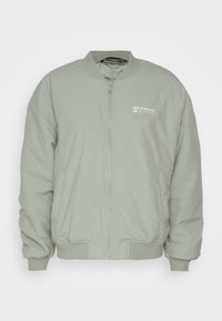 Blouson aviateur vert clair en tissu lisse, doté d'une fermeture éclair à l'avant, d'un col côtelé et d'un petit logo New Balance blanc sur la poitrine.