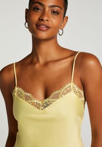 Gul satin camisole med justerbara spaghetti-stängar, med en scalloped spetskant längs halsringen och en slät textur.