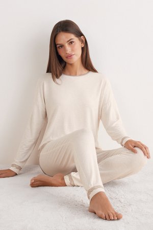 Conjunto de ropa de casa beige que incluye una camiseta de manga larga y pantalones a juego. Tejido suave con un borde decorativo de encaje en los puños y la cintura.