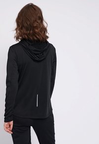Czarna sportowa bluza z kapturem na sznurku, gładka w dotyku, z odblaskowym akcentem na dolnej części pleców. Posiada długie rękawy i luźny krój.
