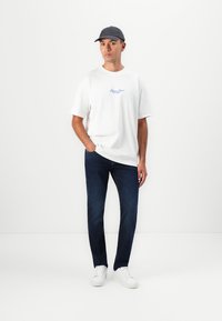 Weißes Baumwoll-T-Shirt mit blauer Schrift, dunkelblaue Jeans, graue Mütze und weiße Sneakers. Lässiger Schnitt mit einem einfachen Design ohne Muster.